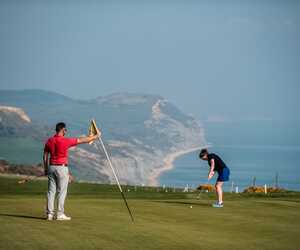 A man teaches a young boy how to hold a golf club outdoors.
